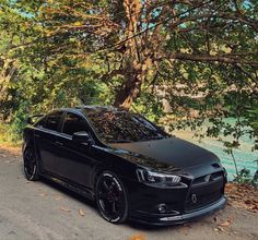 a black car parked on the side of a road next to a tree and water