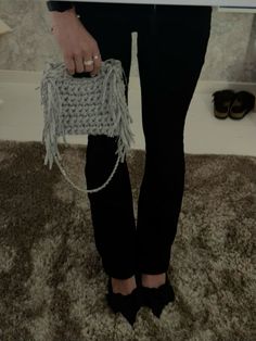 a woman in black pants and heels holding a white purse with fringes on it