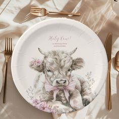 a plate with an image of a cow on it and gold cutlery next to it