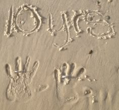 the word joy written in sand with two handprints and an animal's paw