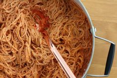 a large pot filled with noodles and sauce on top of a wooden table next to a spoon