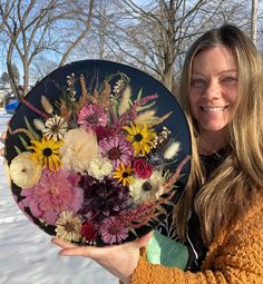 a woman is holding a plate with flowers on it in the snow, smiling at the camera