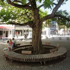 two children sitting on a bench under a tree in the middle of a city square