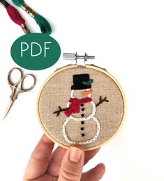 a hand is holding a small embroidery hoop with a snowman on it