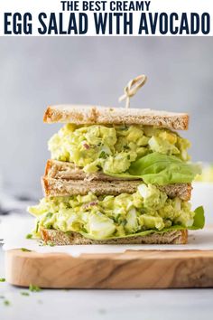 an egg salad sandwich with avocado is stacked on top of a cutting board