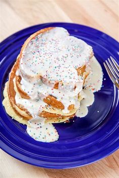 a blue plate topped with pancakes covered in white frosting and sprinkles