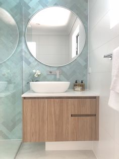 a bathroom with a round mirror above the sink and wooden cabinet below it, along with white towels