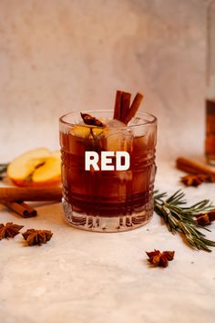 a glass filled with red wine and cinnamon sticks next to an orange slice on the table