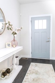 a hallway with a rug, mirror and vase filled with flowers on top of it