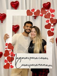 a man and woman pose for a photo in front of a backdrop with red hearts