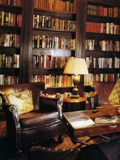 a living room filled with lots of books and leather chairs next to a lamp on a table