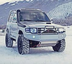 an suv is parked in the snow with mountains in the backgrouds behind it