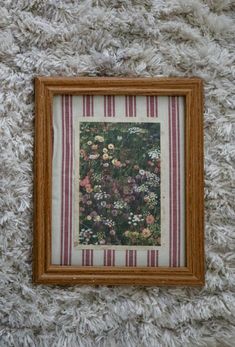 a painting hanging on the wall in a wooden frame with striped fabric around it and flowers