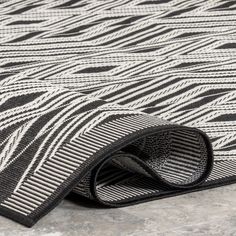 the black and white rug is laying on top of the concrete floor, with an interesting pattern