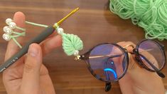 a person holding some yarn and eyeglasses on top of a wooden table next to a pair of glasses