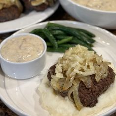 two white plates topped with meat, potatoes and gravy next to green beans