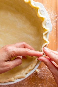 two hands are placing dough into a pie crust