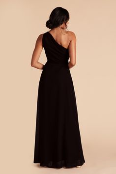 the back of a woman wearing a black dress with one shoulder and open slits