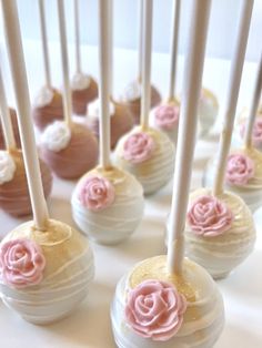 there are many cake pops with pink frosting and roses on them sitting on the table