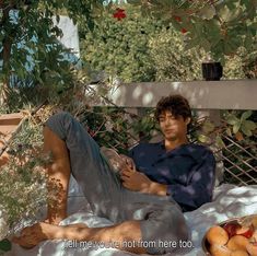 a man sitting on a bed under a tree next to some fruit and vegetables in a bowl