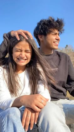 a young man and woman sitting next to each other on a bench with their hair blowing in the wind