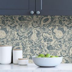 a bowl of green apples sitting on top of a counter next to two white cups