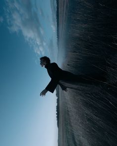 a man standing in front of the ocean with his arms outstretched and head tilted to the side