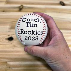 a hand holding a baseball with the words coach tim rockies in black lettering on it