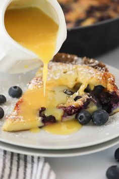 blueberry cheesecake being drizzled with syrup from a pitcher on a plate