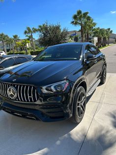 a black mercedes suv is parked on the side of the road in front of some palm trees