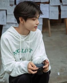 a young man sitting on the ground holding a remote control in his hand and looking at something