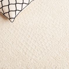 a white and black pillow sitting on top of a beige carpeted floor next to a bed