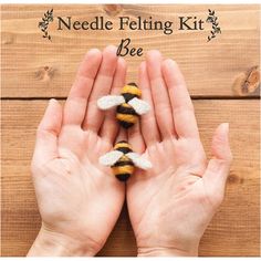 two hands holding small bees on top of a wooden table with the words bee needle felting kit