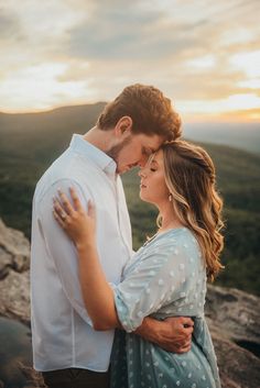 a man and woman standing next to each other on top of a mountain at sunset