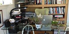 a glass desk topped with a laptop computer next to a book shelf filled with books