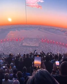 a large group of people standing in front of a stage at sunset with their cell phones