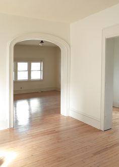 an empty living room with hard wood flooring and large arched doorway leading into another room