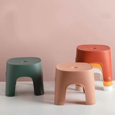 three different colored stools sitting next to each other on a white surface with a pink wall in the background