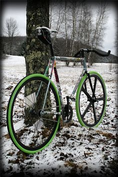 a green and white bike parked next to a tree in the snow with no leaves on it