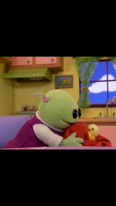 a green stuffed animal holding a red stuffed duck in a room with pink walls and cabinets