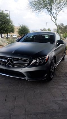 a black mercedes benz coupe parked in front of a building on a brick sidewalk next to trees