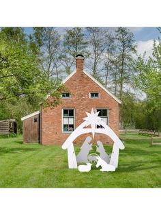 a nativity scene in front of a brick house with trees and grass around it