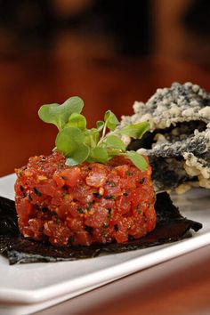 a white plate topped with meat covered in sauce and garnished with green leaves