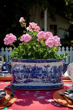 pink flowers are in a blue and white pot on a table with plates, silverware and utensils