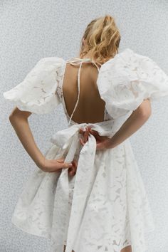 the back of a woman wearing a white dress with an open neckline and ruffled sleeves