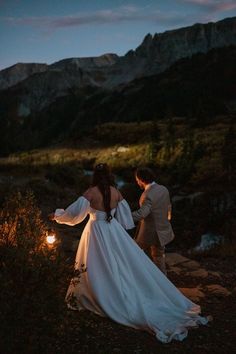 the bride and groom are walking in the mountains at night with their arms spread out