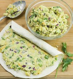 a wooden table topped with a burrito covered in cheese and vegetables next to a bowl of guacamole