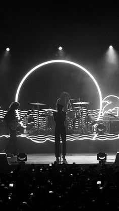 two people are standing on stage with their backs turned to the side and lights behind them