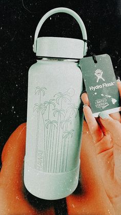 a hand holding a water bottle with a tag attached to it and palm trees on the label