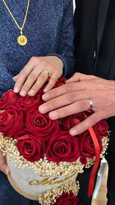 two people holding a bouquet of red roses with gold accents on their hands and wedding rings